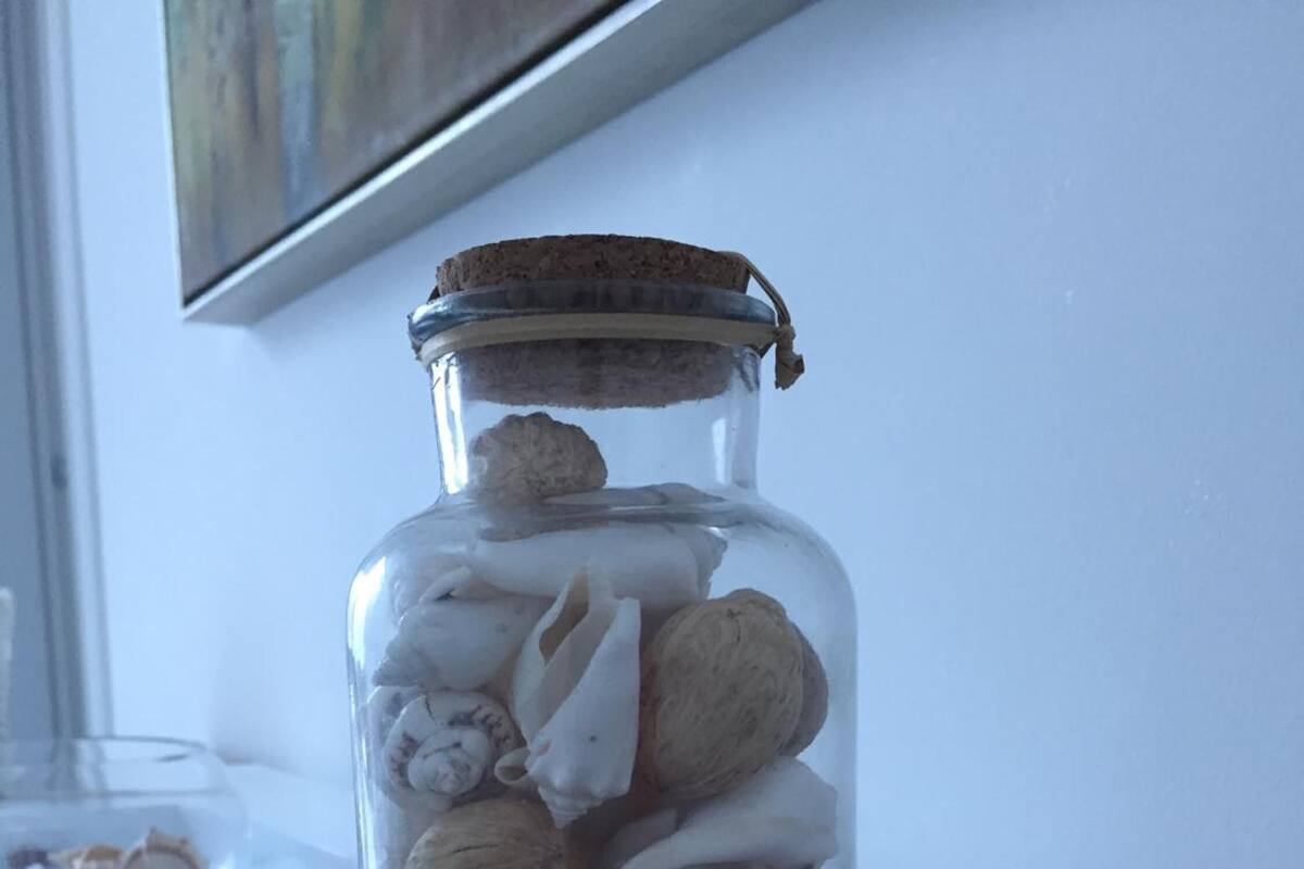 A glass jar with a metal lid containing various seashells and driftwood on a wooden surface.
