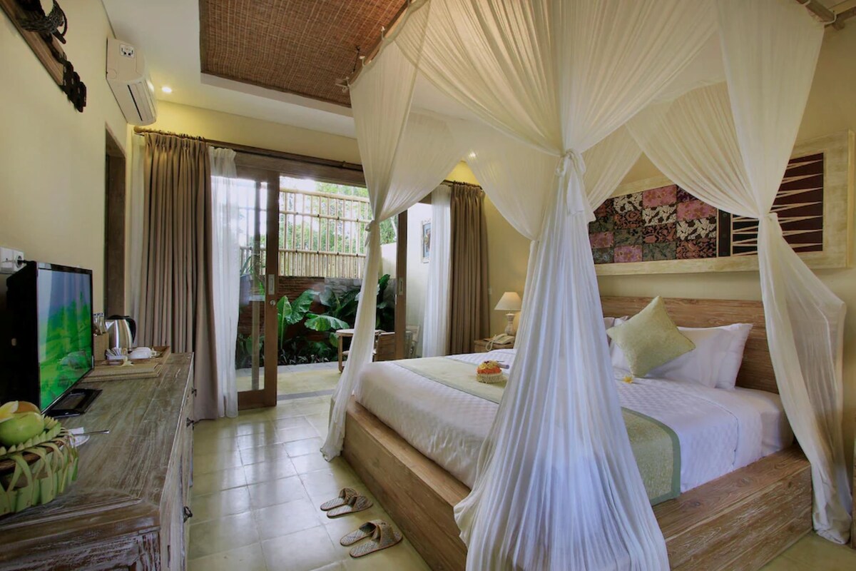 A bedroom with a bed, curtains, a television, and a wooden bench.