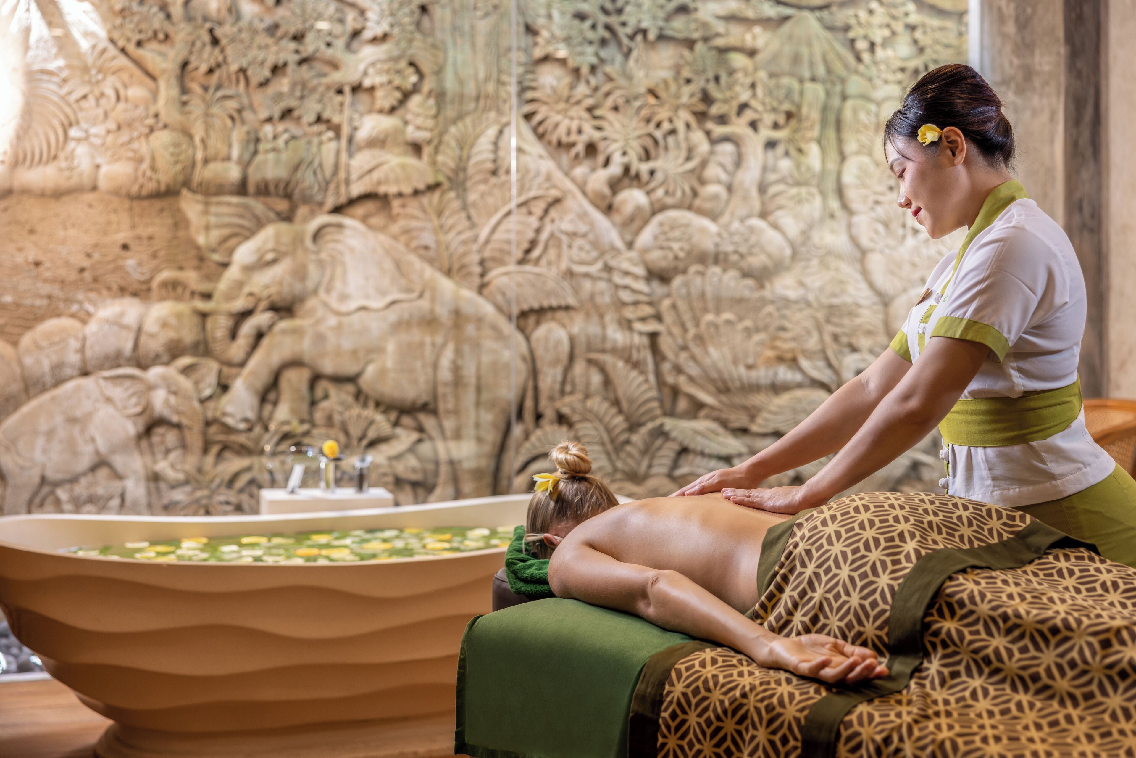 A massage therapy session in a room with a large bathtub and a detailed stone wall mural.