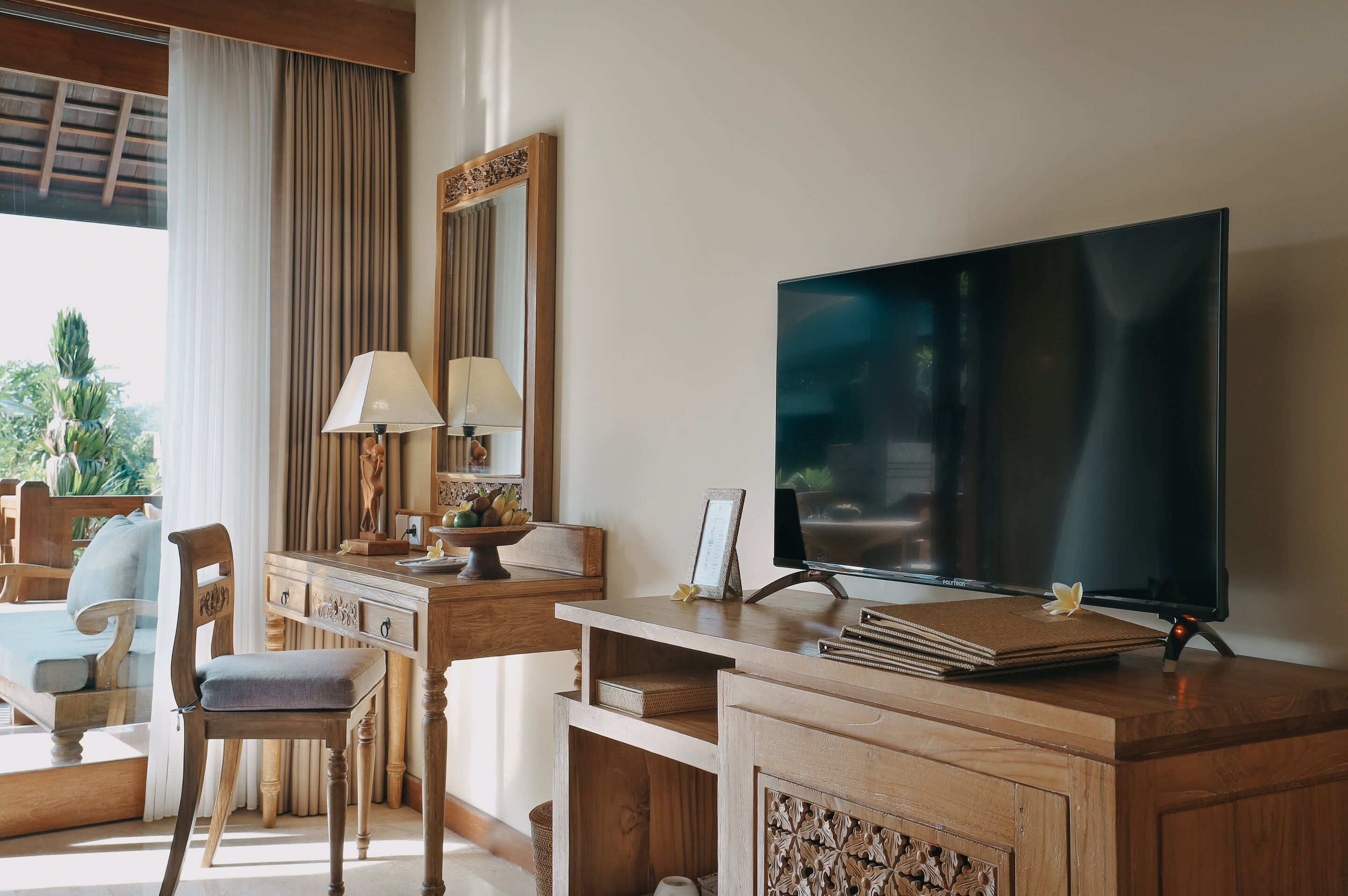 A hotel room with a wooden desk, a television, a chair, and a window with curtains.