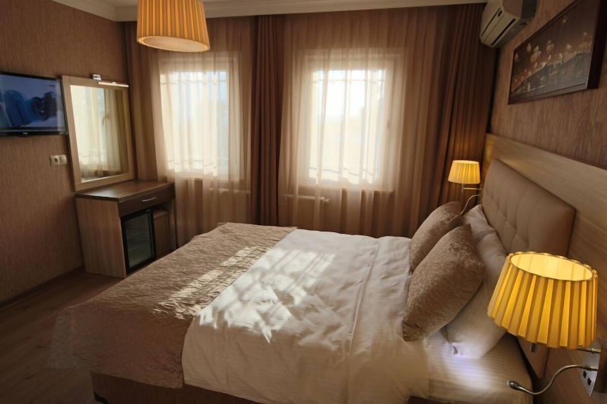A hotel room with a bed, bedside lamps, a TV, a mirror, and curtains.
