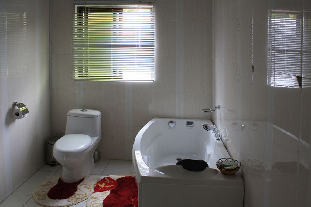 A bathroom with a toilet, a bathtub, and a window with blinds.