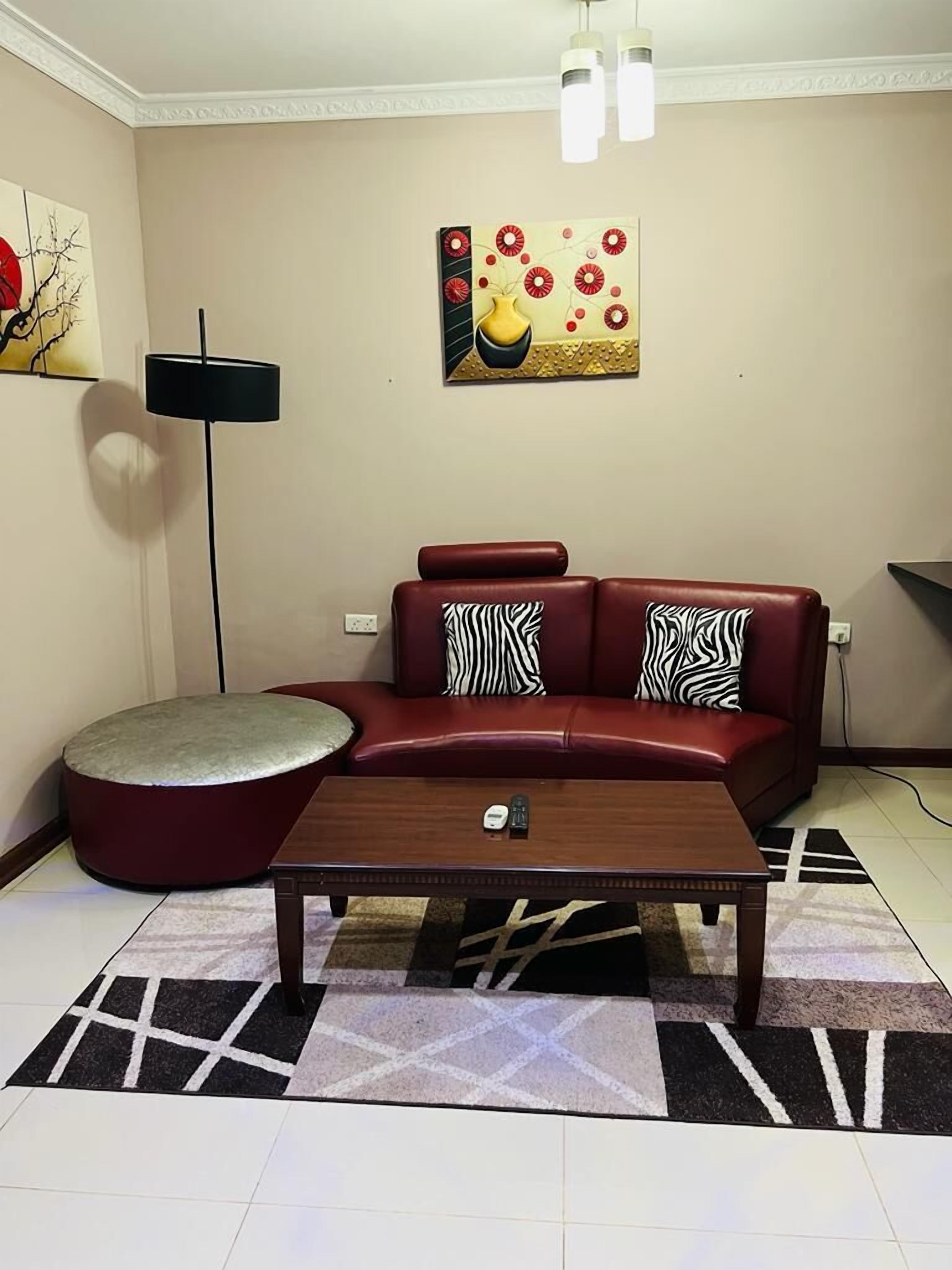 A living room with a red sofa, a round ottoman, a coffee table, and a painting on the wall.