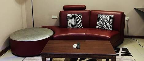 A living room with a red sofa, a round ottoman, a coffee table, and a painting on the wall.