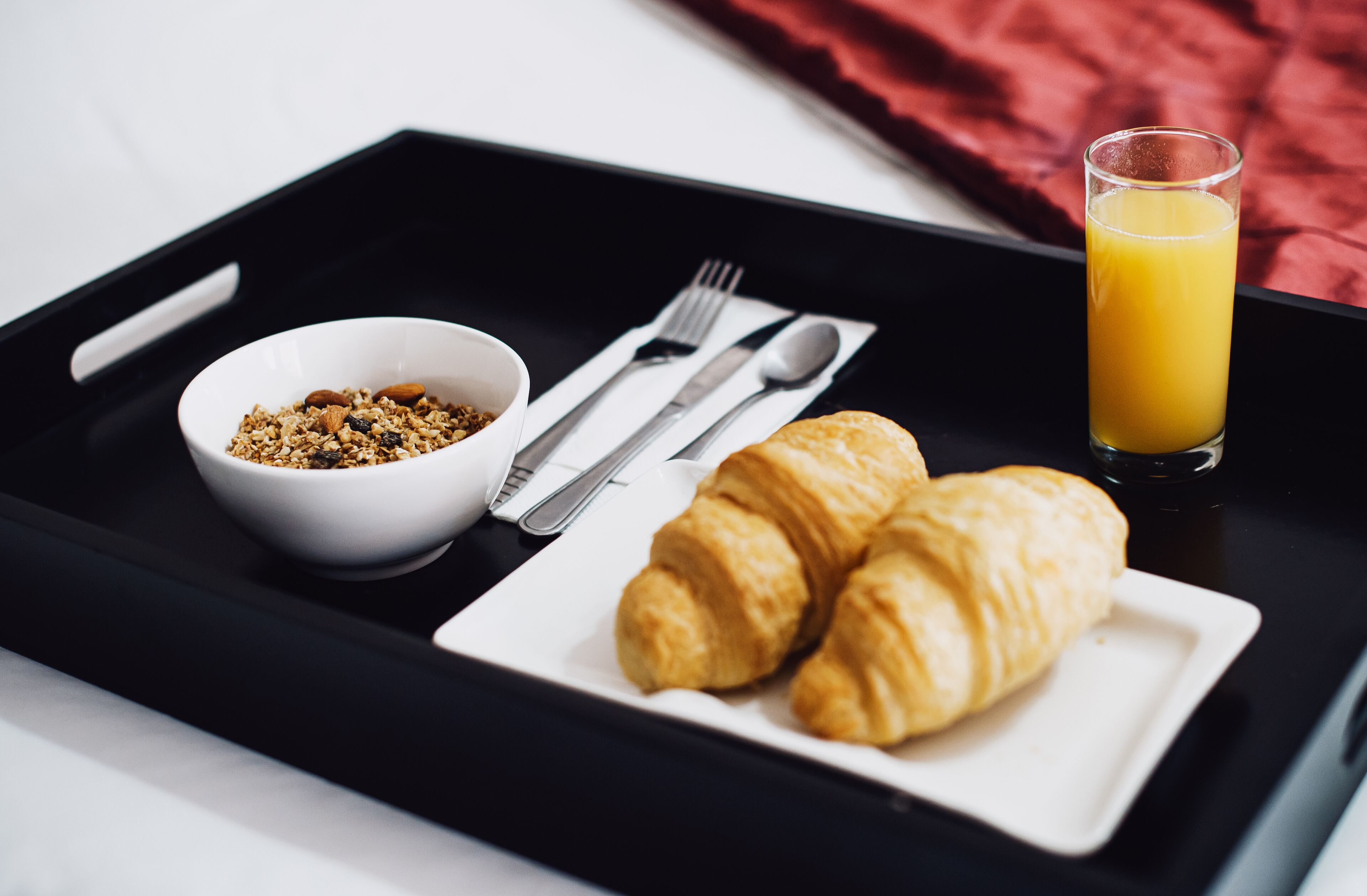 A breakfast tray with a bowl of granola, two croissants, cutlery, and a glass of orange juice.