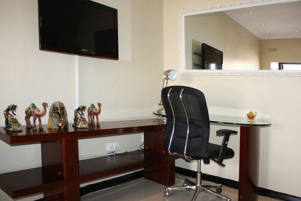 A hotel room with a wooden desk, a black office chair, a flat-screen TV, a mirror, and decorative camel figurines.