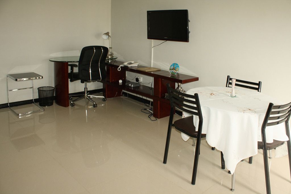 A small, clean room with a desk, a chair, a TV mounted on the wall, and a table with chairs.
