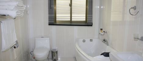 A bathroom with a toilet, a bidet, a bathtub, and a window with blinds.