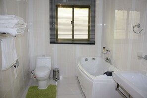 Bathroom features a white bathtub, toilet, and window with horizontal blinds.