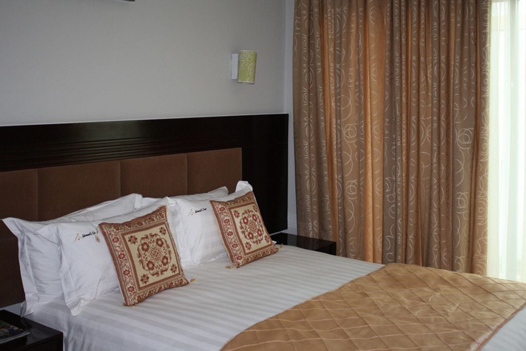 A hotel room with a bed, two pillows, a nightstand, and a window with curtains.