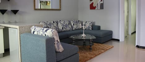 A modern living room with a grey sofa, a glass coffee table, and a decorative rug.