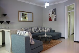 A modern living room with a grey sofa, a glass coffee table, and a decorative rug.