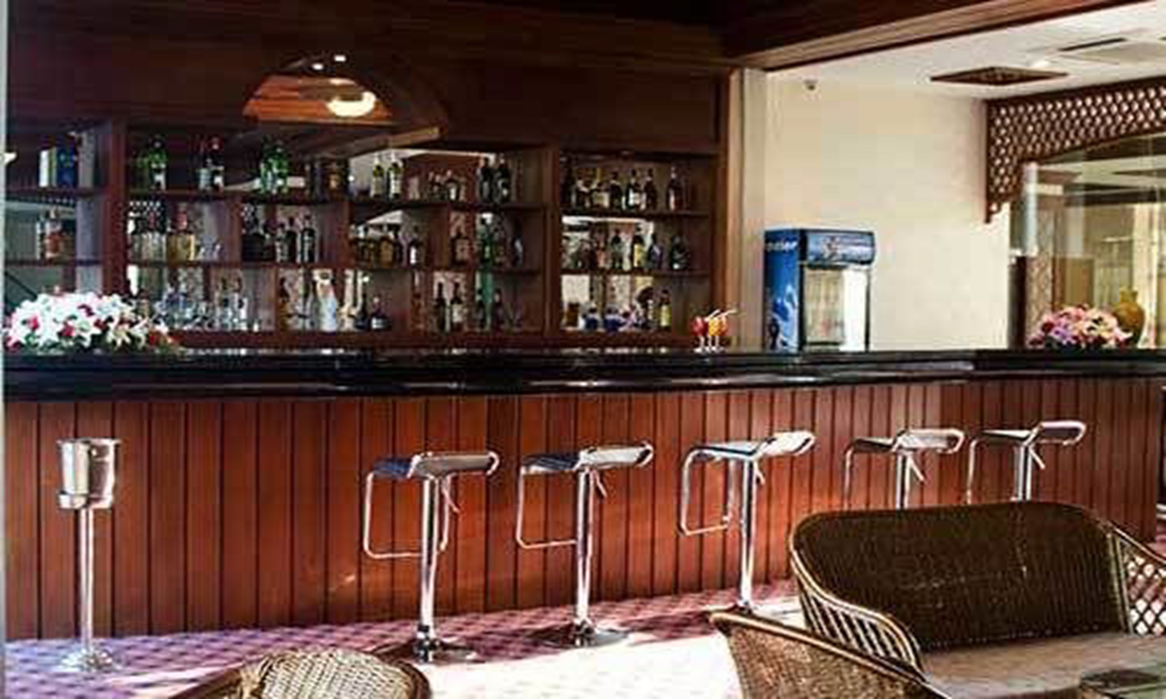 Zona de bar con paneles de madera, taburetes y una barra con diferentes botellas.