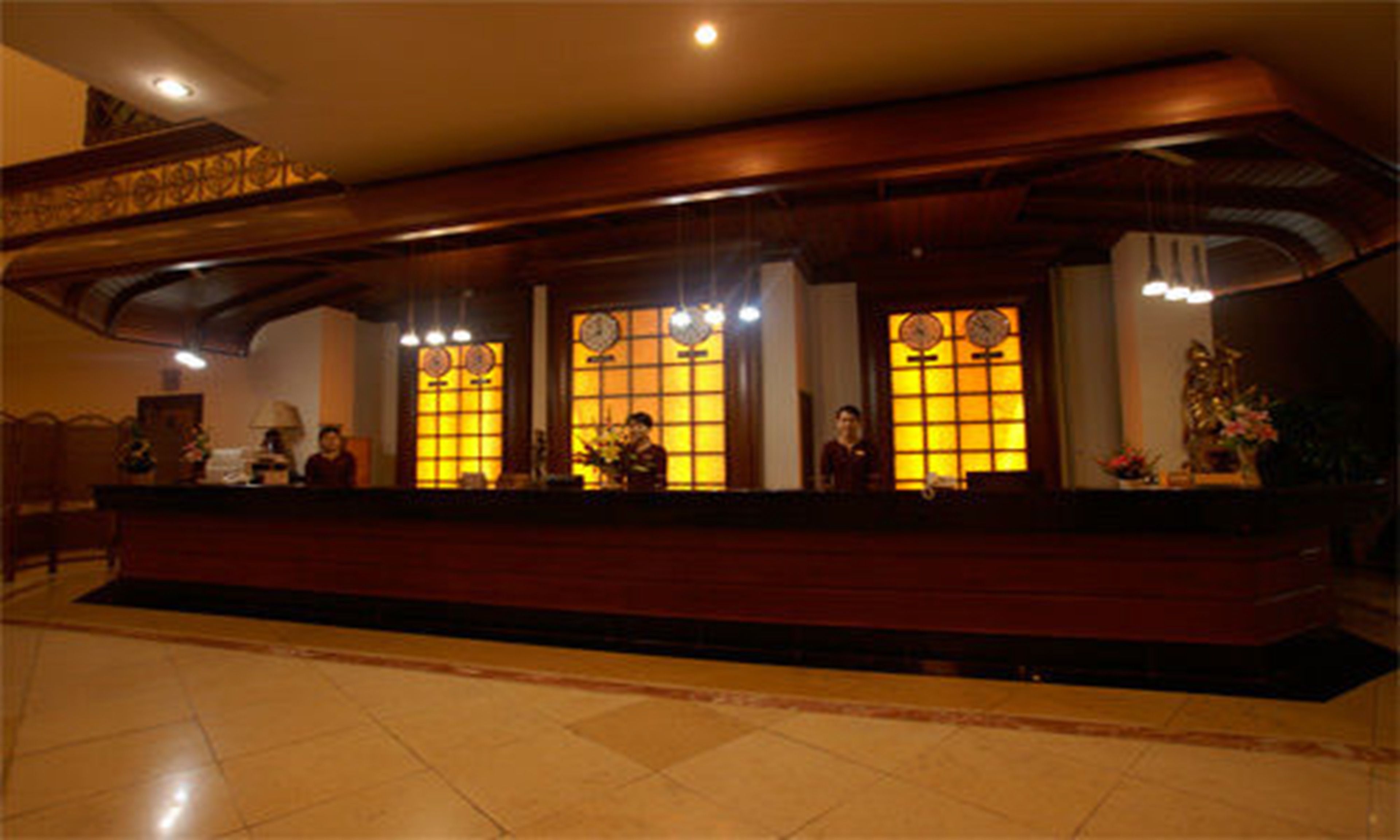 A reception area with a wooden reception desk, two large windows with clocks, and a tiled floor.