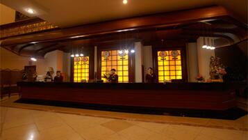 A reception area with a wooden reception desk, two large windows with clocks, and a tiled floor.