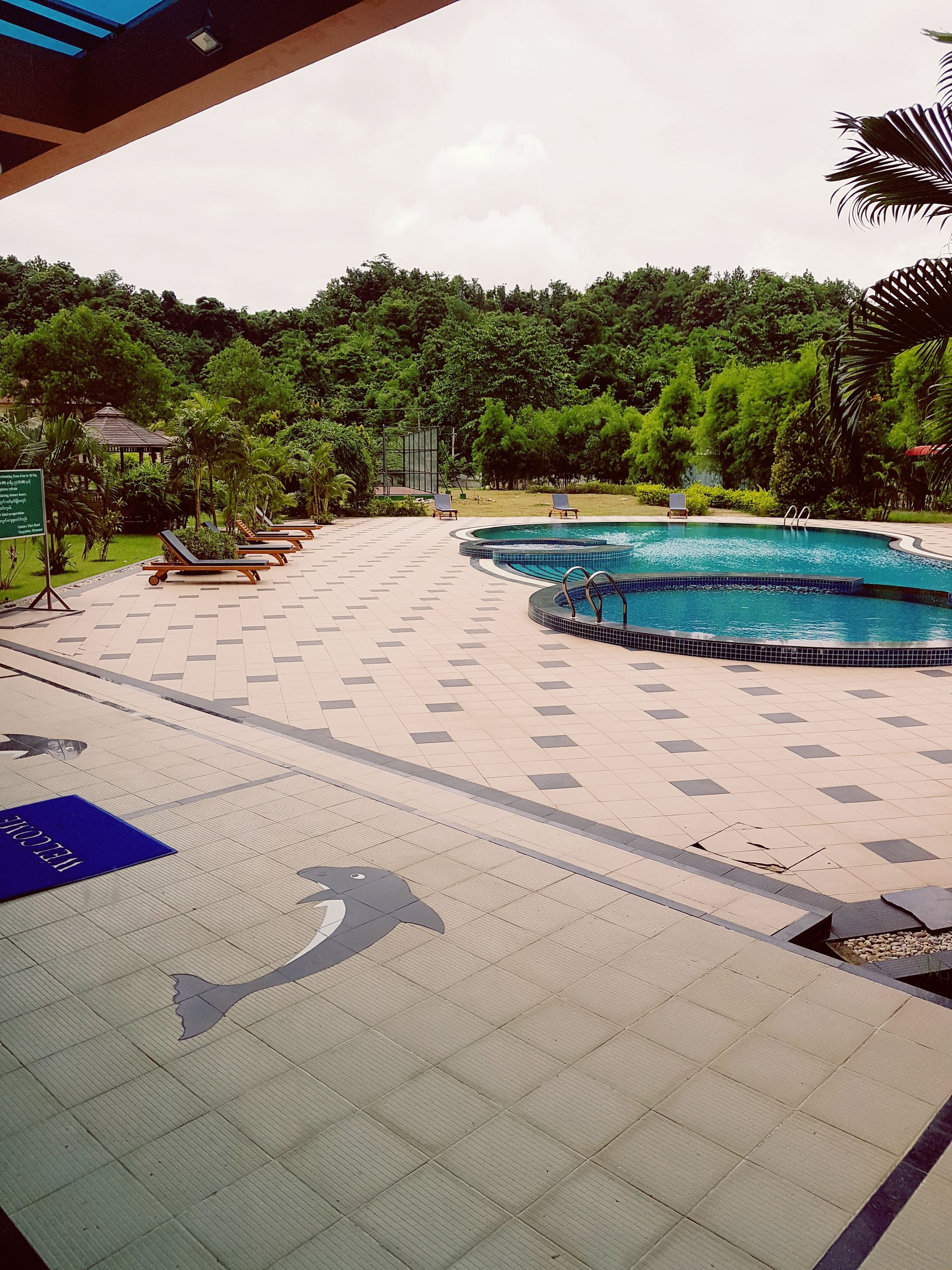Zona de piscina con sillas de descanso, piscina y cartel.