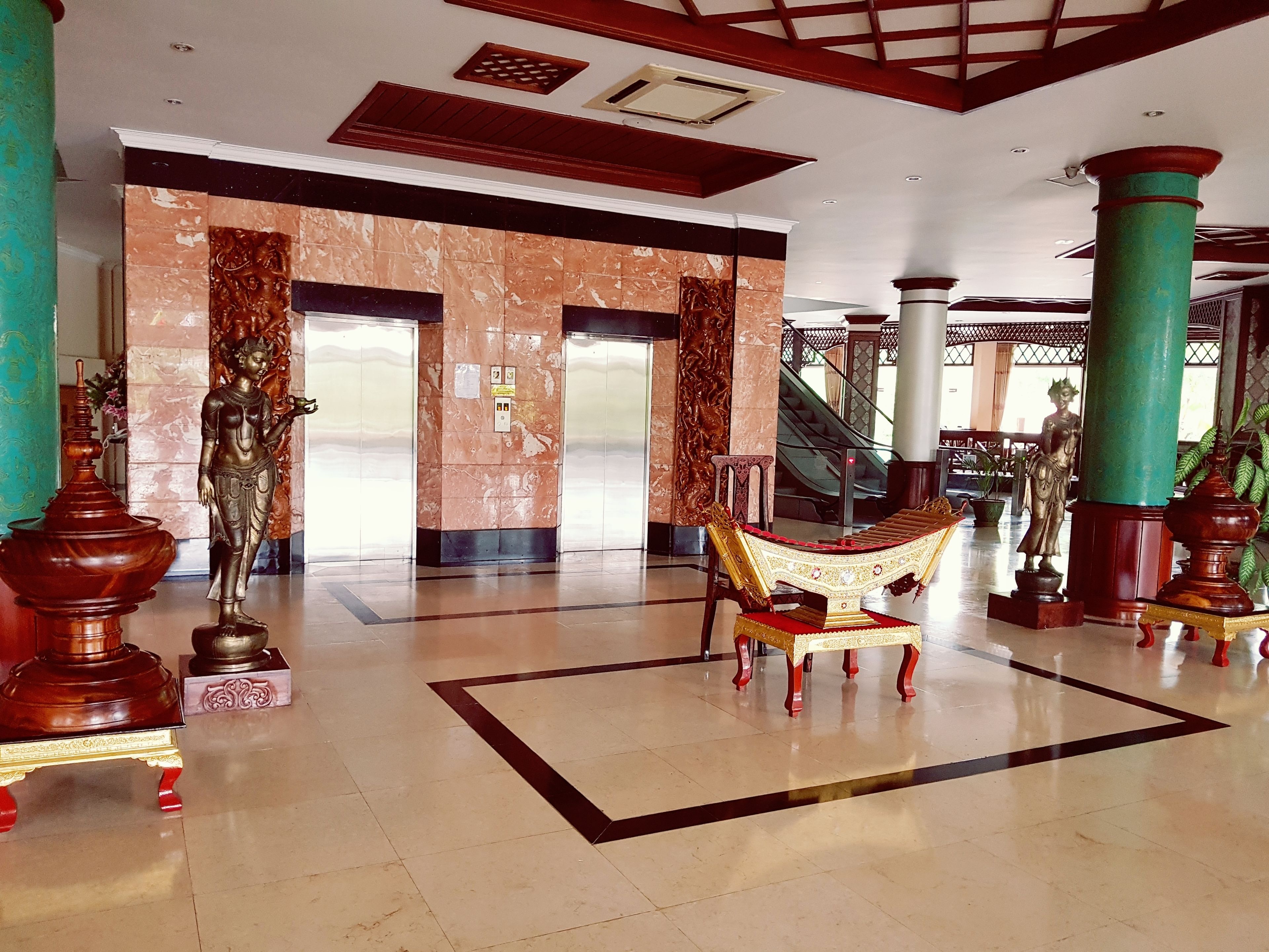 A spacious lobby with marble flooring, a central ornate chair, and a statue.