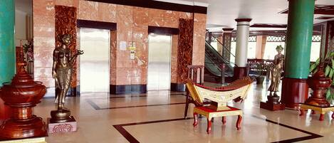 A spacious lobby with marble flooring, a central ornate chair, and a statue.