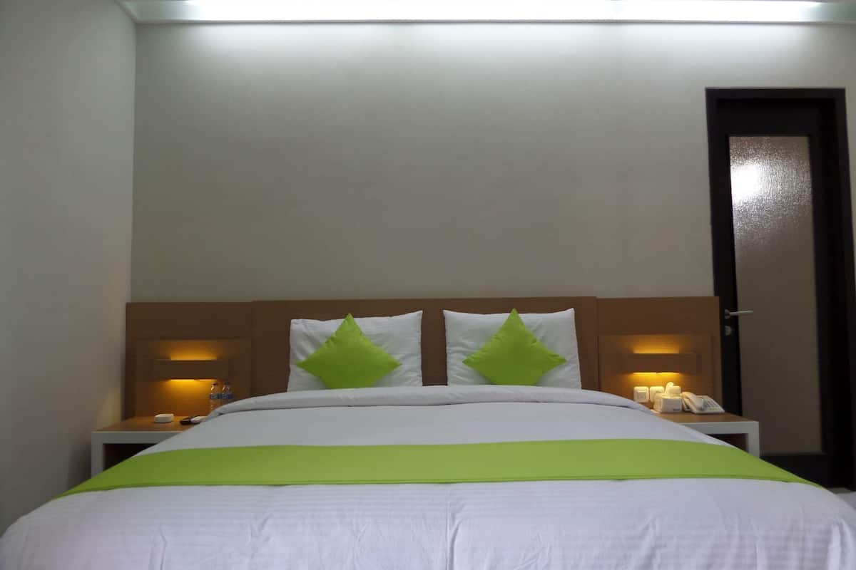 Quarto de hotel com uma cama, duas mesas de cabeceira, um criado-mudo, uma porta e um candeeiro fixado na parede.