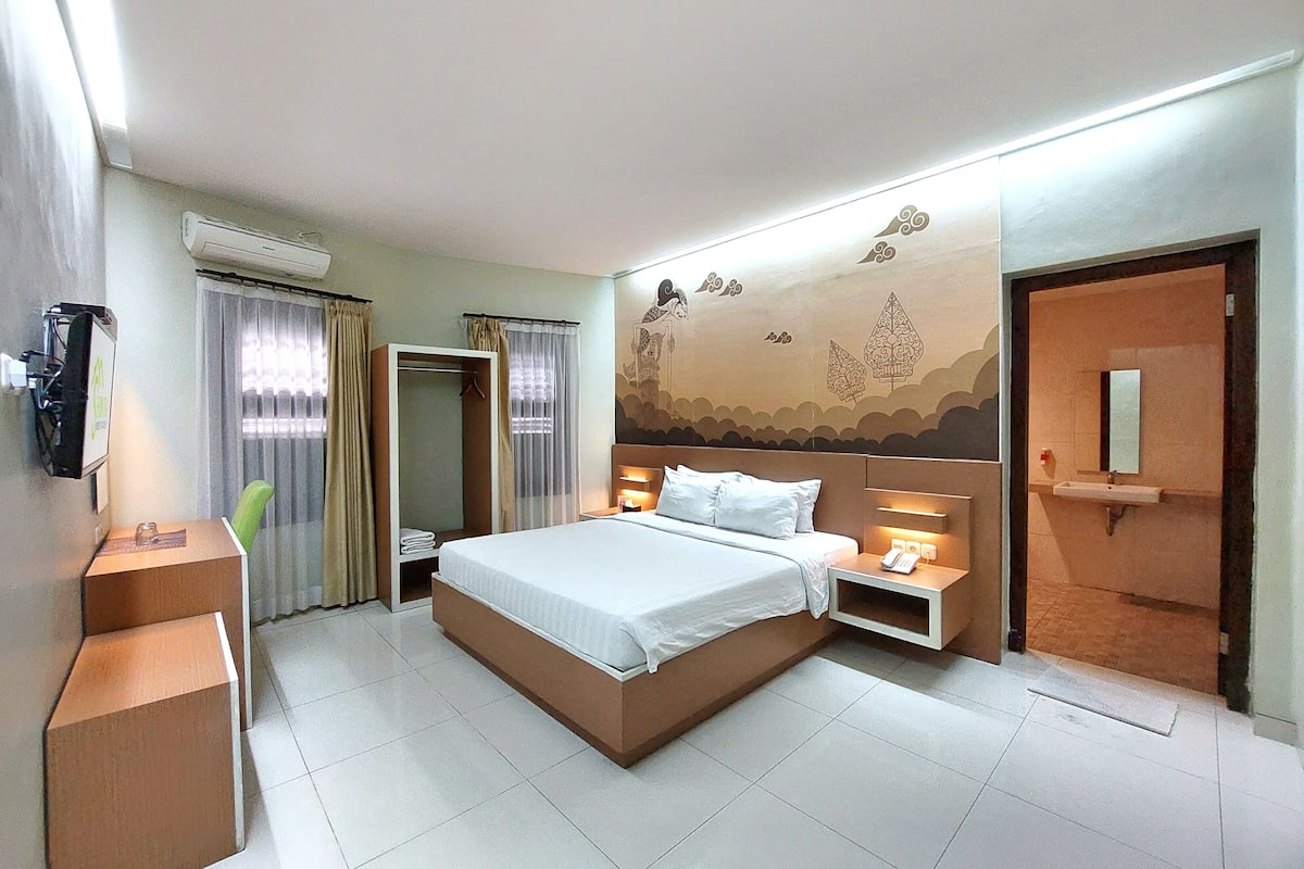 Quarto de hotel com cama, mesa de cabeceira, luminária e espelho.