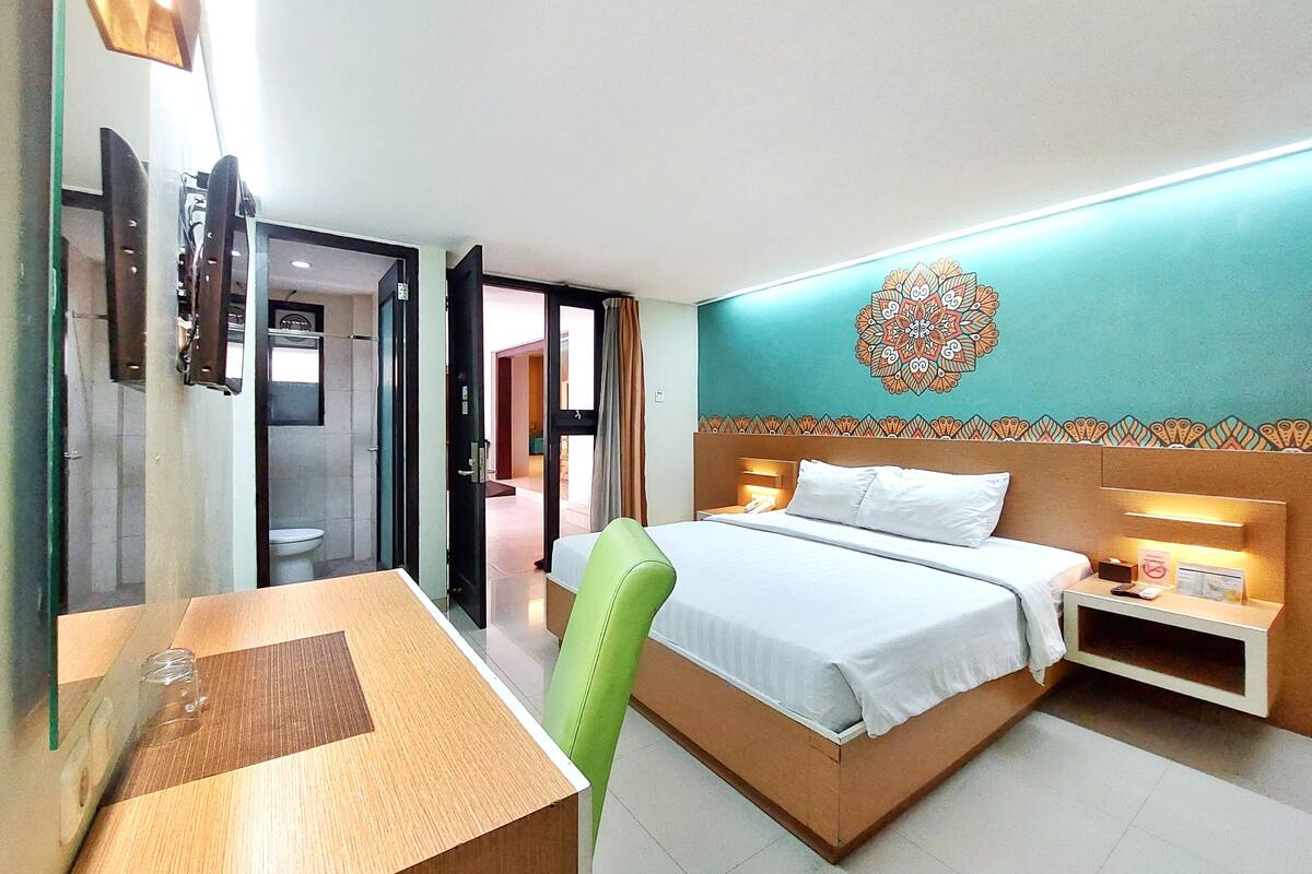 Quarto de hotel com cama, mesa de cabeceira e escrivaninha com cadeira.