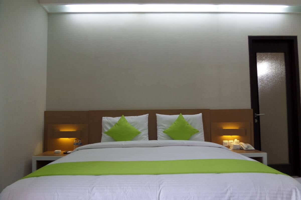 Quarto de hotel com cama, duas mesas de cabeceira, telefone e porta.