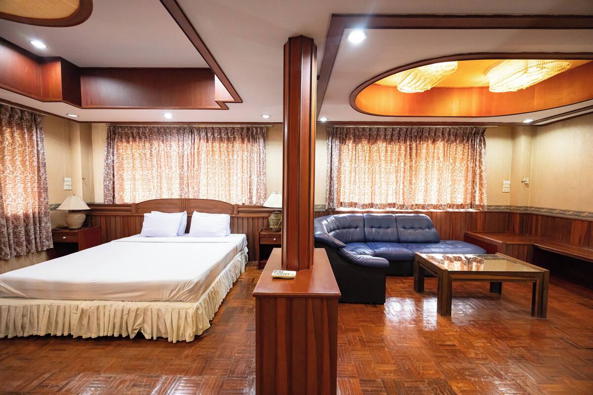 A hotel room with a large bed, a leather sofa, a wooden coffee table, and a chandelier.