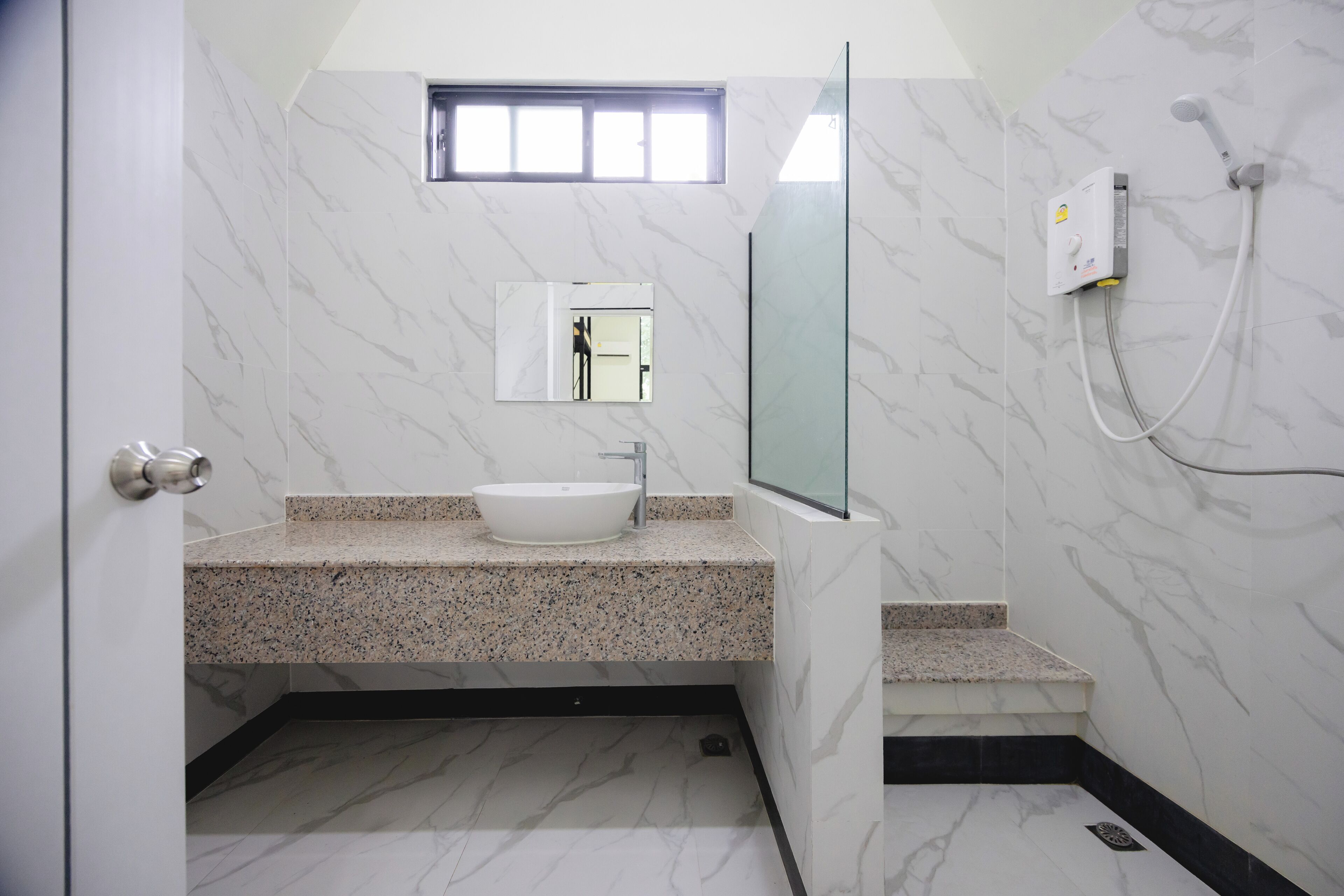 A modern bathroom with a white marble floor, a granite countertop, a white sink, a glass shower enclosure, and a small window above the mirror.