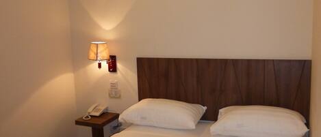 Ein Hotelzimmer mit einem Bett, zwei Kissen, einem Nachttisch mit Lampe und Telefon sowie einem Holz-Kopfteil.