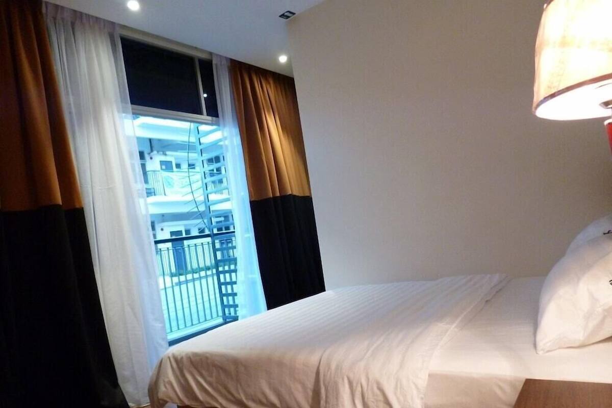 A hotel room with a bed, a bedside telephone, and a window with curtains.