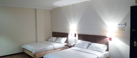 Habitación de hotel con dos camas individuales, suelo de madera y una pared blanca lisa.