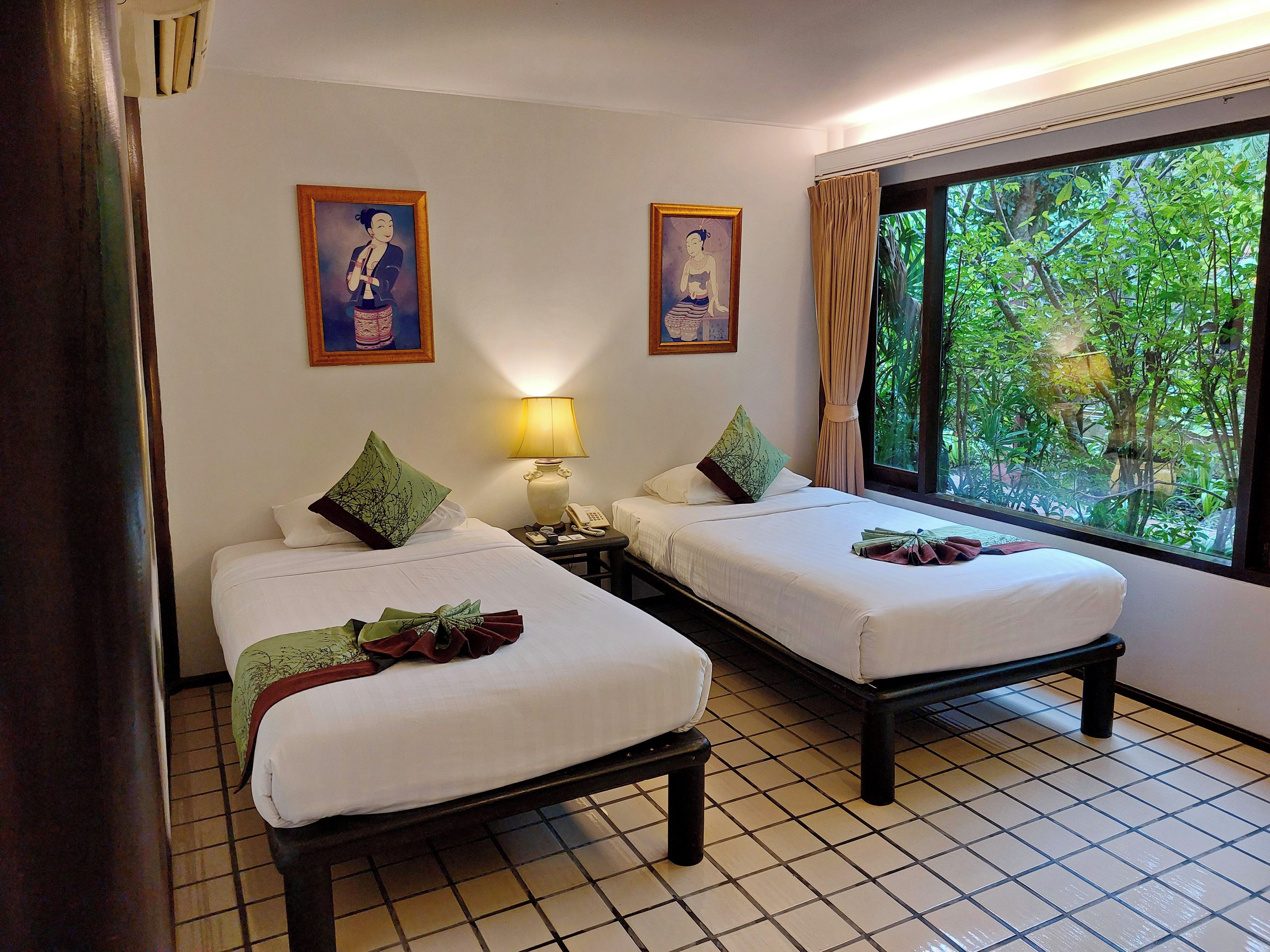 Habitación de hotel con dos camas, una mesita de noche con lámpara, teléfono y ventana con cortinas.