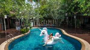 Una piscina con un flotador de unicornio, rodeada de árboles y un área de descanso.