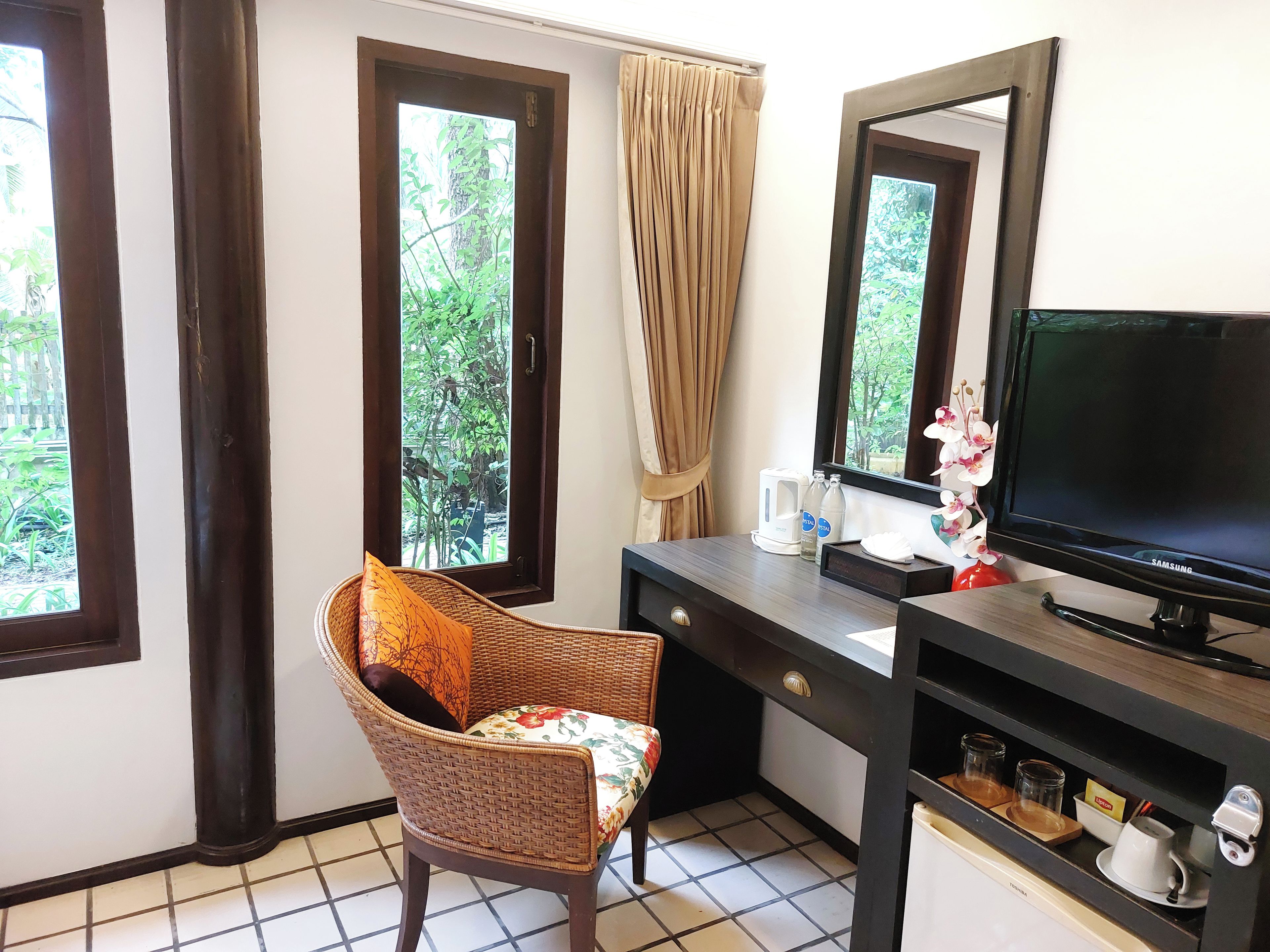 A hotel room with a television, a desk with a kettle, a chair, and a window with curtains.
