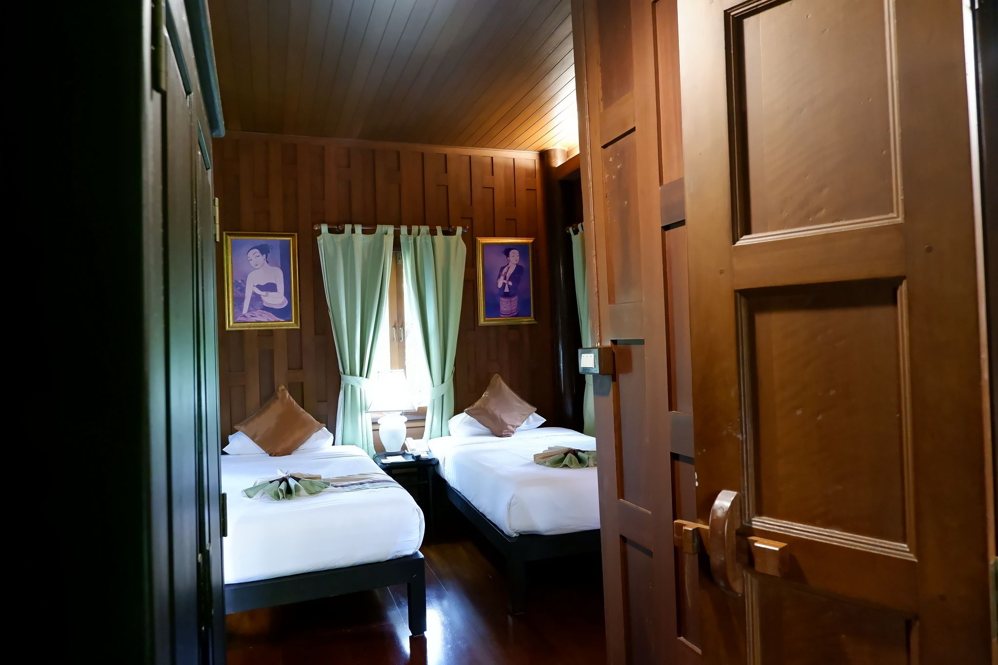 Een hotelkamer met twee bedden, houten lambrisering en twee ingekaderde foto's aan de muur.