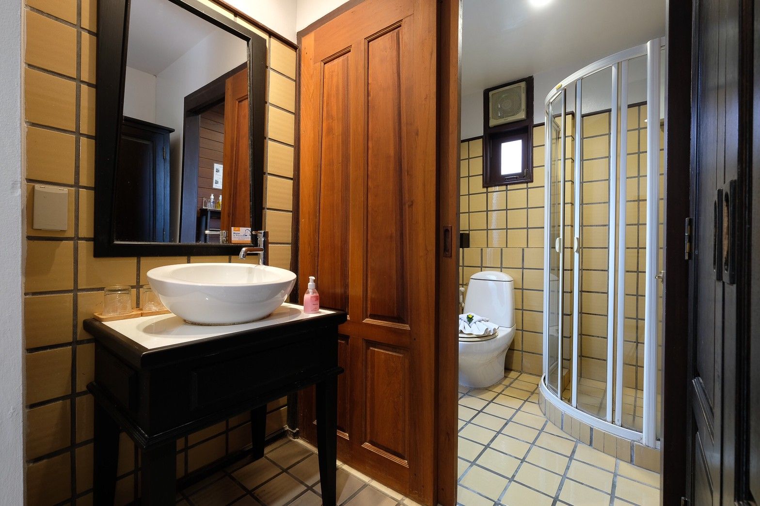 Un baño con lavamanos blanco, tocador de madera y cabina de ducha de vidrio.
