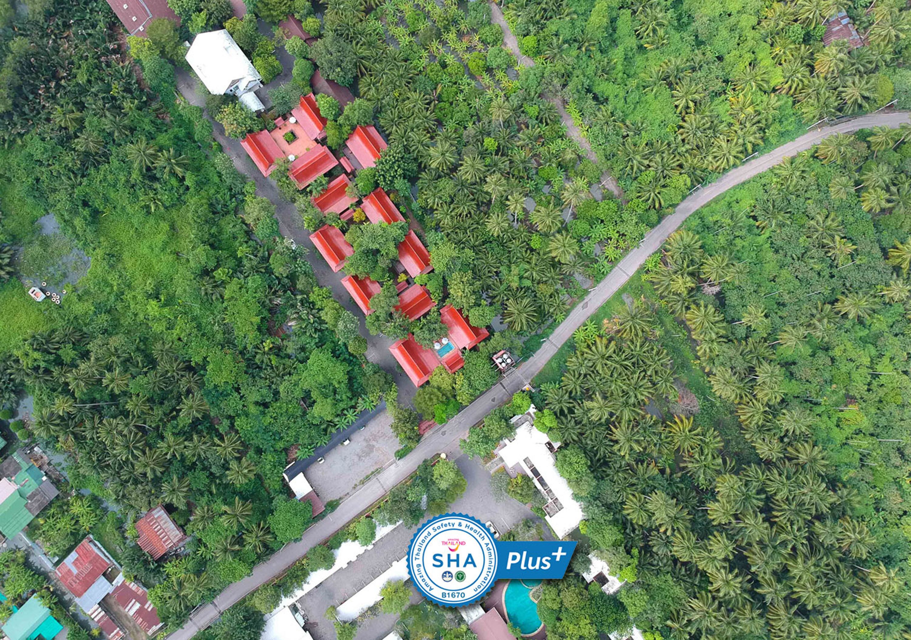 An aerial view of a residential area with multiple red-roofed buildings surrounded by dense greenery and palm trees.
