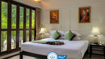 A hotel room with a large bed, two wall-mounted paintings, a window with curtains, and two bedside lamps.
