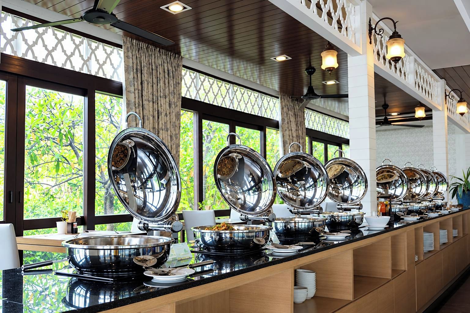 Buffet montado com diversas estações de serviço, um balcão longo e vista para o verde lá fora.