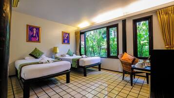 Habitación de hotel con dos camas, una mesa de comedor, televisión y ventanas amplias con vistas a zonas verdes.