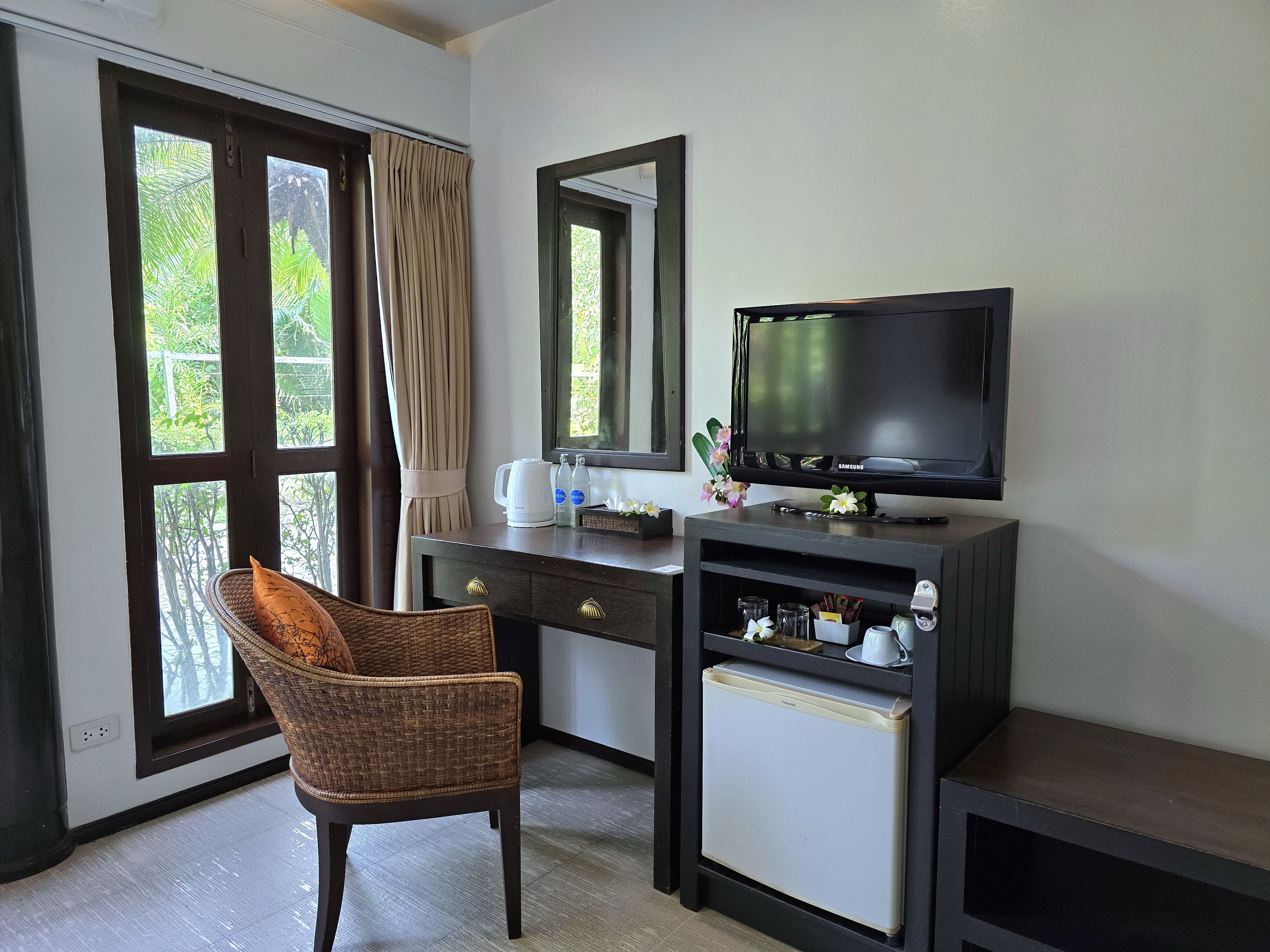 A hotel room with a desk, a television, a chair, and a window with curtains.