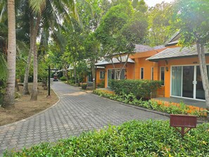 A pathway leading to a row of orange buildings with a paved walkway and lush greenery. - Baan Amphawa Resort & Spa (Amphawa)
