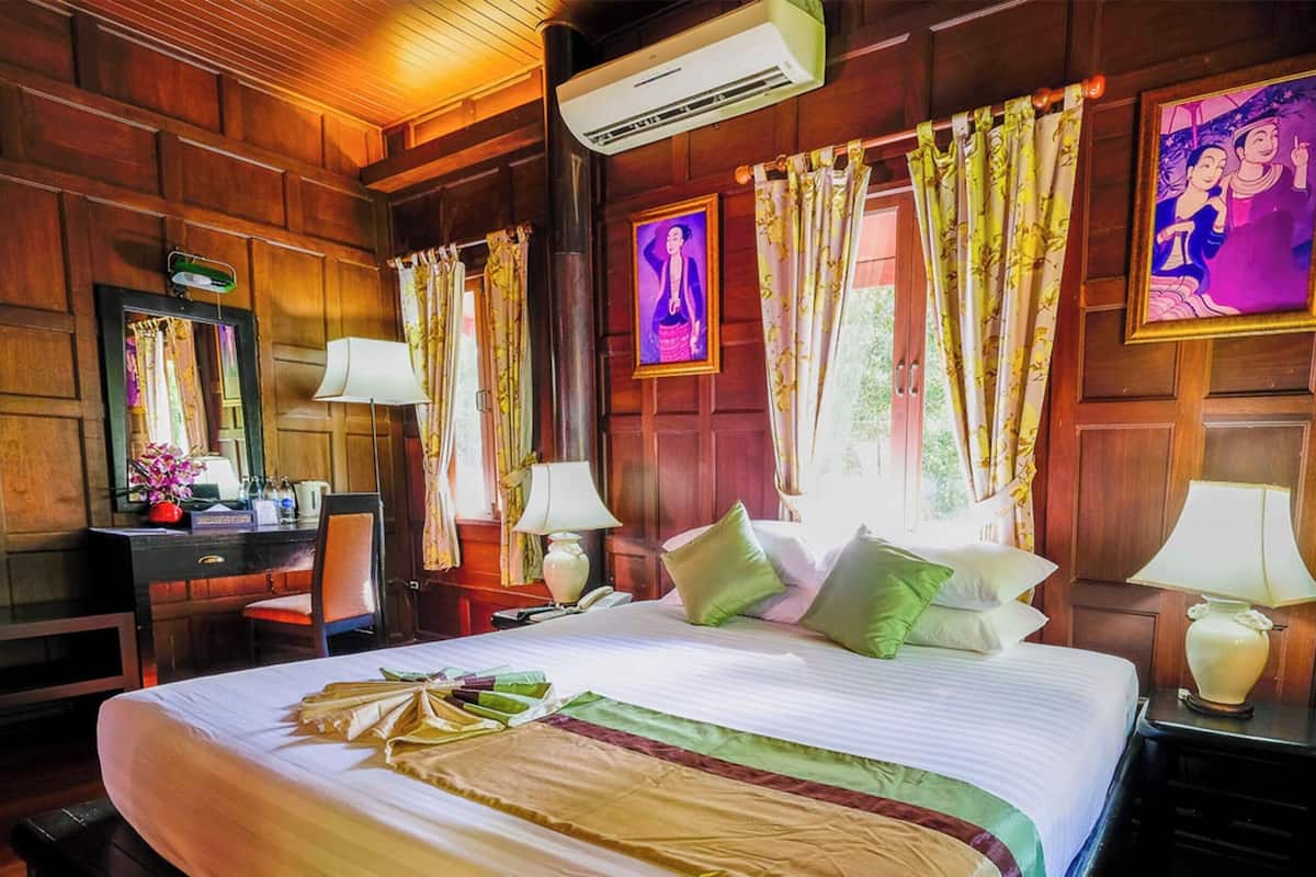 Habitación de hotel con una cama grande, paredes de madera, un escritorio con silla, dos mesitas de noche con lámparas y un espejo.