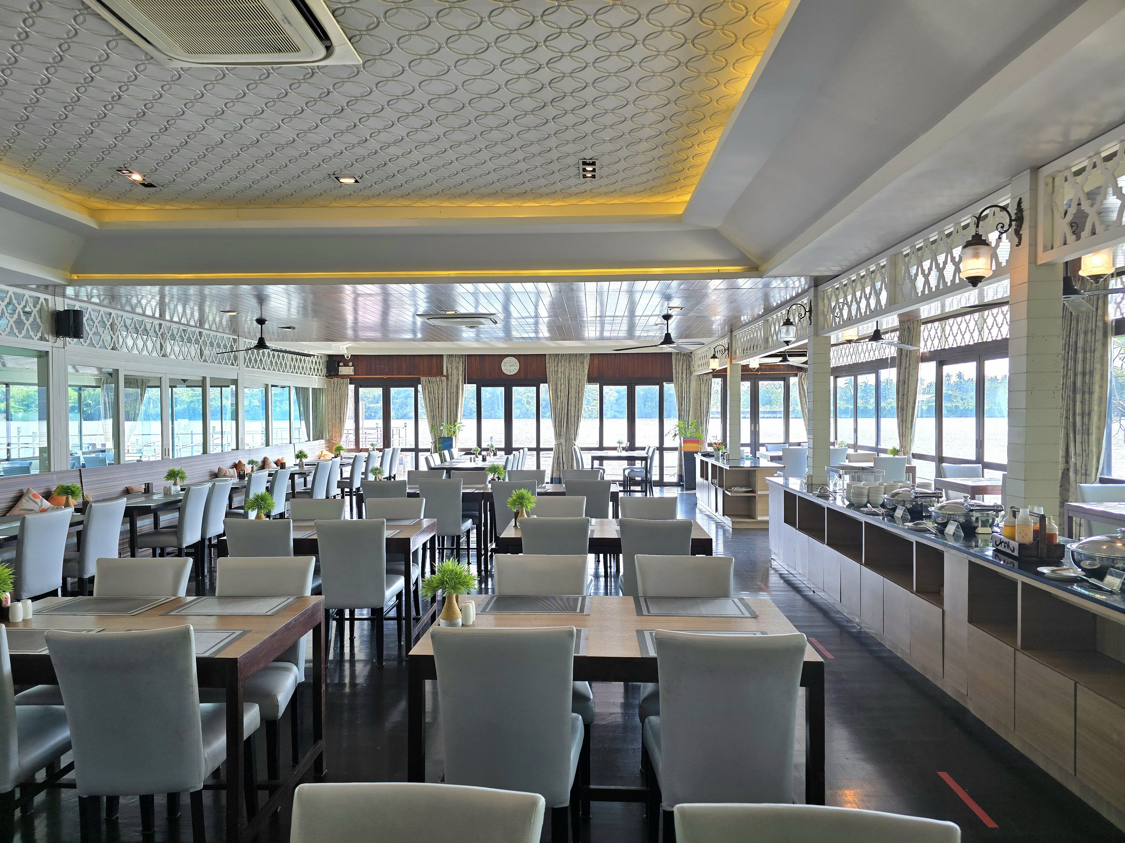 A spacious restaurant with multiple dining tables and chairs, large windows, and a decorative ceiling.
