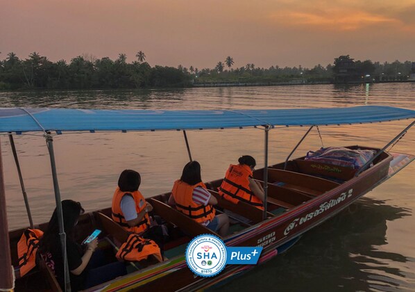 A boat with passengers wearing life jackets, a blue canopy, and a logo indicating safety certification. - Baan Amphawa Resort & Spa (Amphawa)