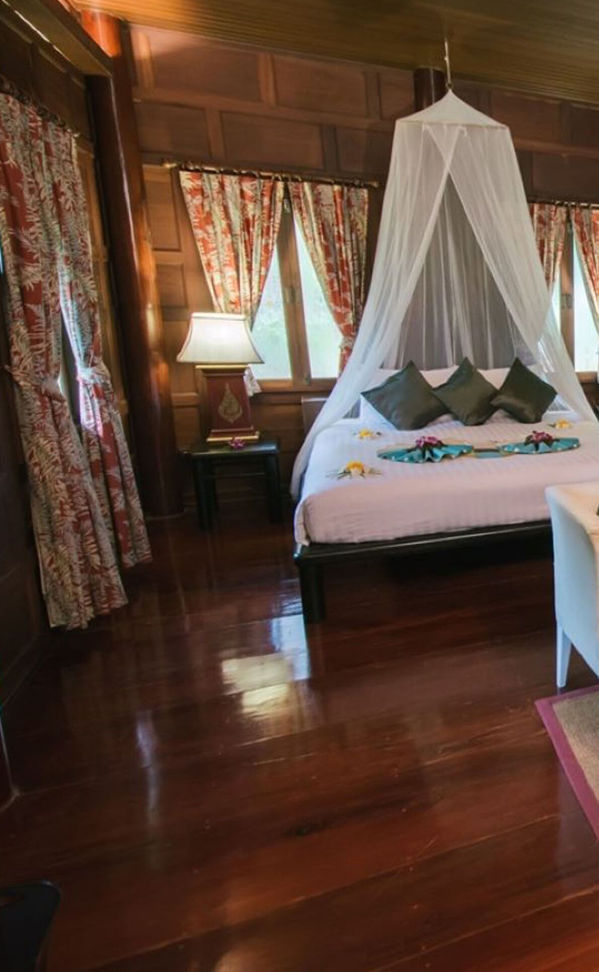 A bedroom with a canopy bed, wooden flooring, and floral curtains.