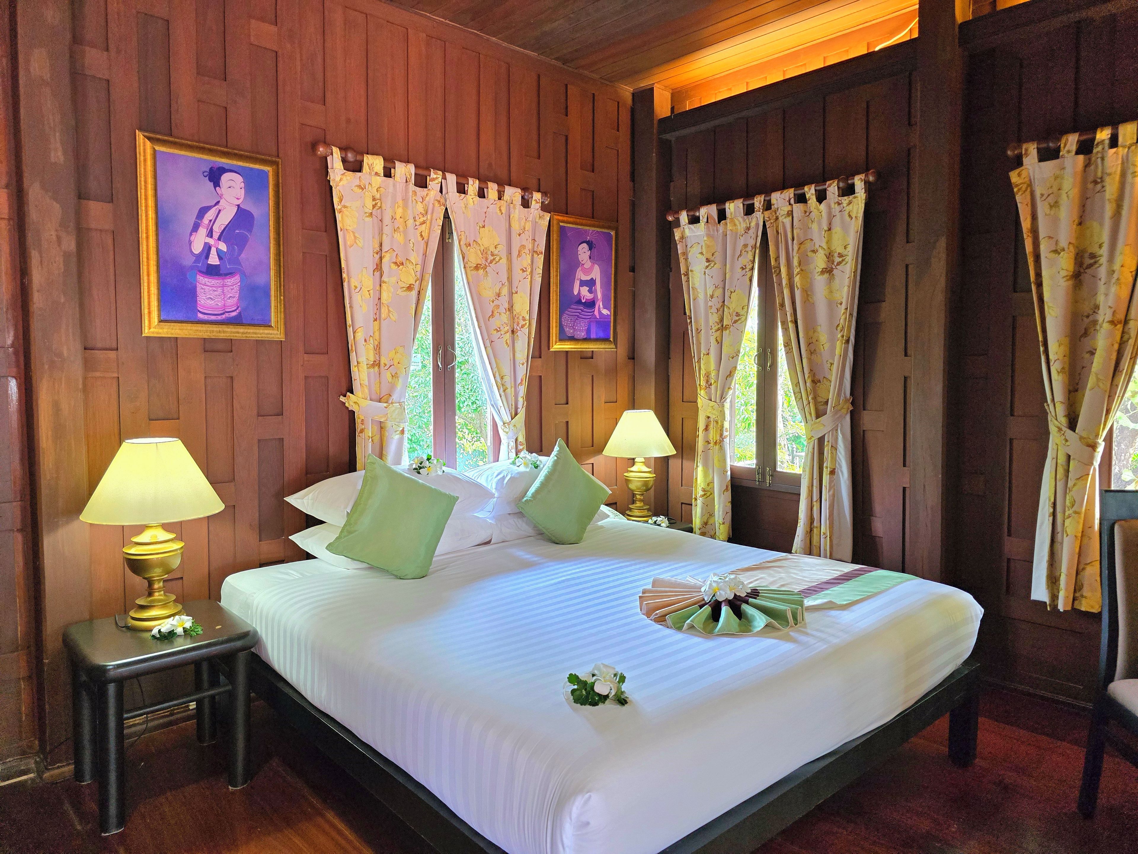 Habitación de hotel con una cama grande, dos mesitas de noche con lámparas, cortinas florales y paneles de madera.