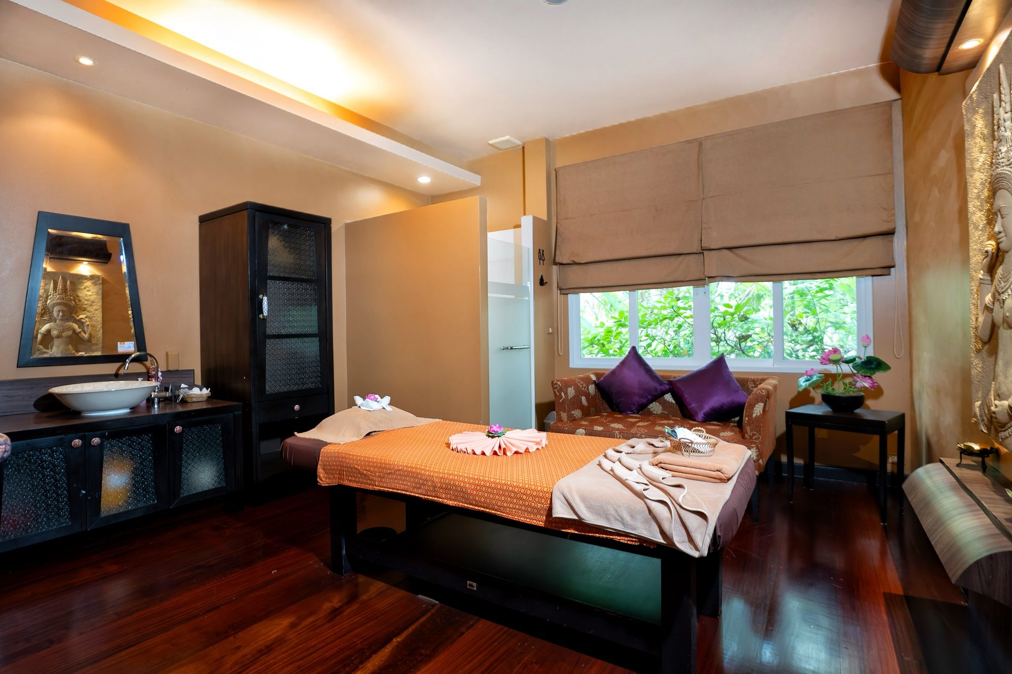 Habitación de hotel con cama, zona de estar, ventana con vista a zonas verdes, baño con lavamanos y espejo, y un armario.