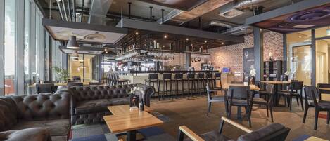 A modern bar area with leather seating, a bar counter, and exposed ductwork on the ceiling.