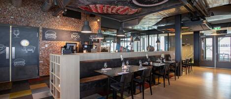 Un restaurante moderno con pared de ladrillo, una zona de bar y un área de mesas y sillas.